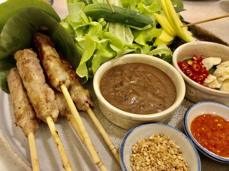 หมูสับย่างเสียบไม้ไผ่ วางคู่ผักสลัด มะม่วงดิบ น้ำจิ้มถั่ว และพริก